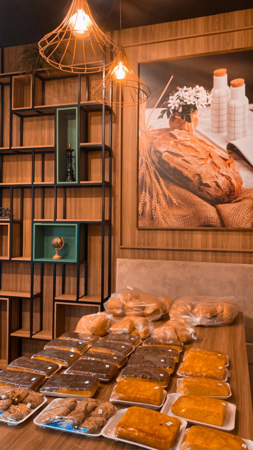 Mesa com bolos e pães embalados sob luminárias de cobre